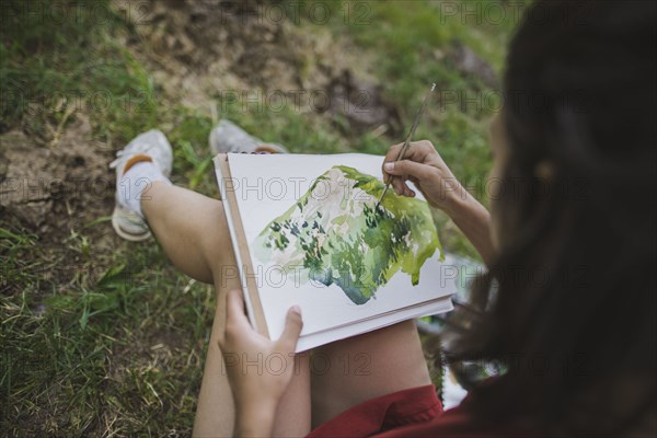 Switzerland, Obergoms, Young woman painting with watercolor in Swiss Alps