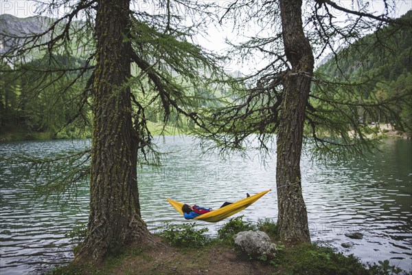 Switzerland, Bravuogn, Palpuognasee, Young woman resting in hammock near Palpuognasee lake in Swiss Alps