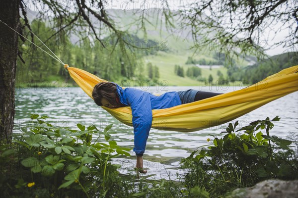 Switzerland, Bravuogn, Palpuognasee, Young woman resting in hammock near Palpuognasee lake in Swiss Alps