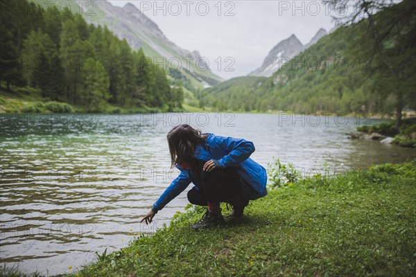 Switzerland, Bravuogn, Palpuognasee, Young woman crouching by Palpuognasee lake in Swiss Alps