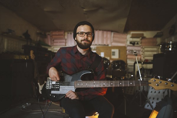 Young man playing bass guitar during rehearsal in garage