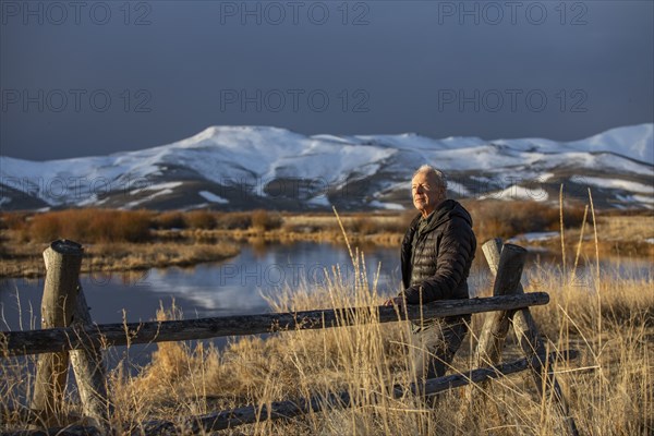USA, Idaho, Sun Valley, Senior man leaning against fence looking at view