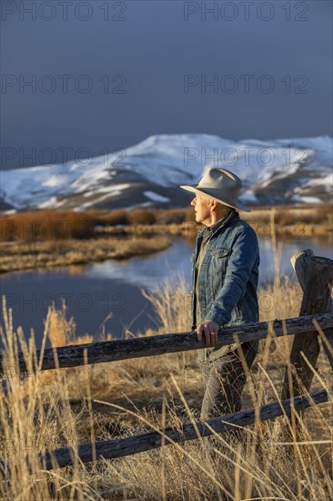 USA, Idaho, Sun Valley, Senior man leaning against fence looking at view