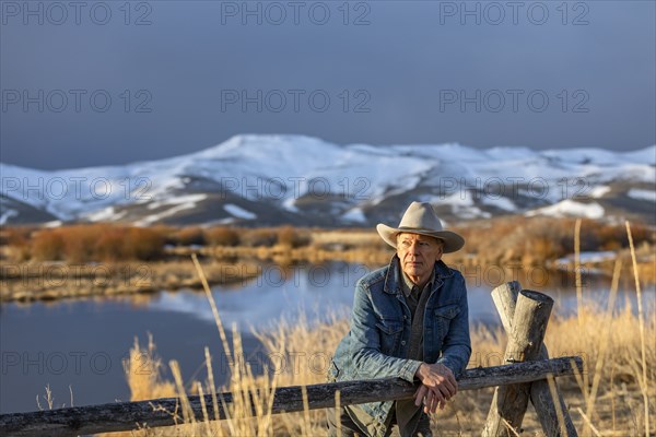 USA, Idaho, Sun Valley, Senior man in cowboy hat leaning against fence