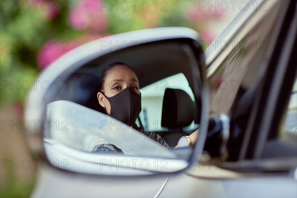 Woman with face mask driving car reflected in mirror