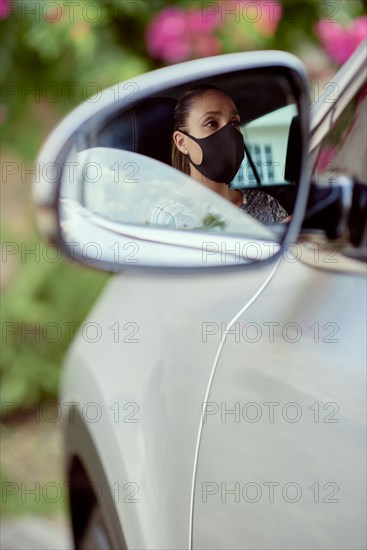 Woman with face mask driving car reflected in mirror