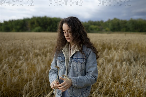 Russia, Omsk, Young woman standing in wheat field and holding wheat