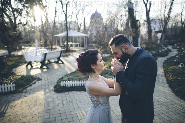 Groom kissing hands of his newlywed wife in garden