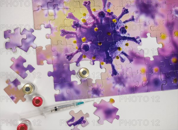 Studio shot of puzzle with Coronavirus model and vaccine vials and syringe