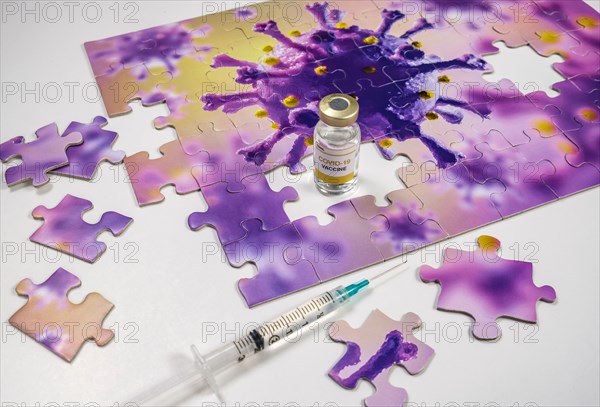 Studio shot of puzzle with Coronavirus model and vaccine vials and syringe