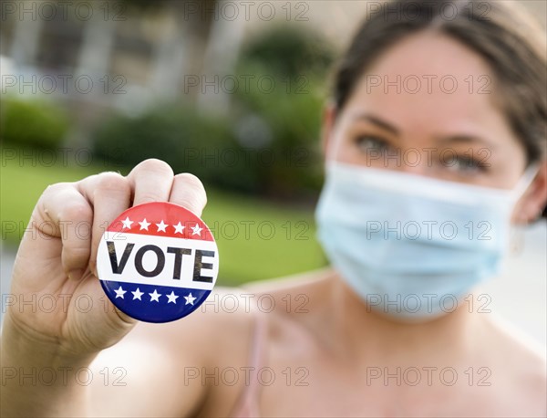 Portrait of women wearing face mask holding Vote button