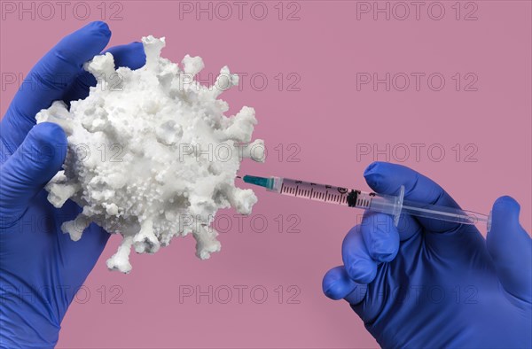 Hands in blue latex gloves holding Coronavirus model and syringe