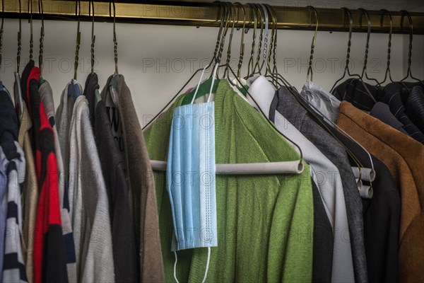 Surgical mask hanging on hanger on rack with clothes