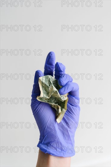 Studio shot of hand in latex glove holding crumpled dollar bill
