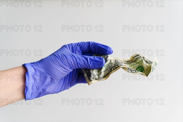 Studio shot of hand in latex glove holding crumpled dollar bill