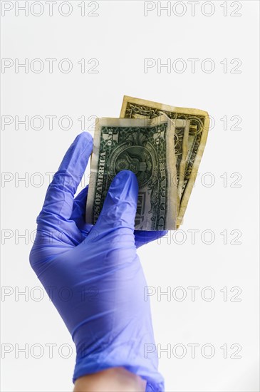 Studio shot of hand in latex glove holding folded dollar bills