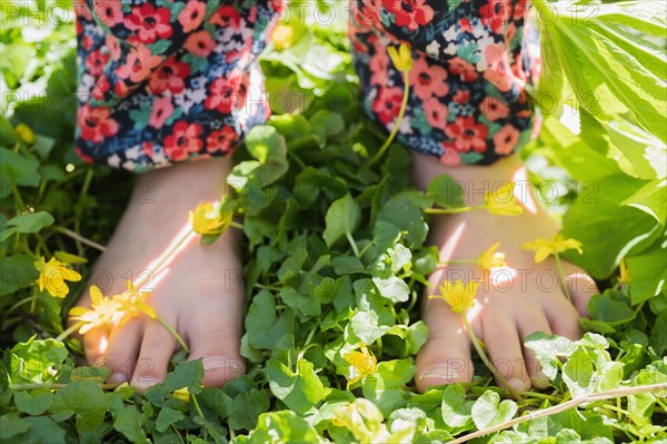 Close-up of girls (6-7) bare feet standing on meadow with yellow flowers