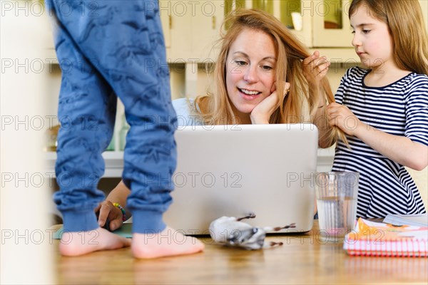 Woman working on laptop while son (4-5) and daughter (6-7) distracting her