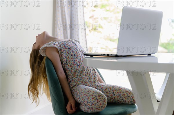 Girl (6-7) leaning back on chair while remote learning