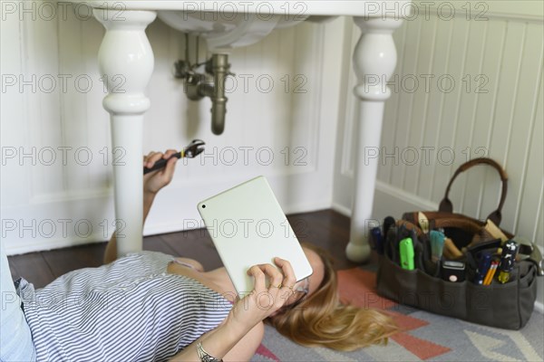 Woman repairing sink while watching DIY tutorial on laptop