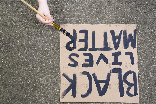 Woman's hand painting Black Lives Matter sign on cardboard,,