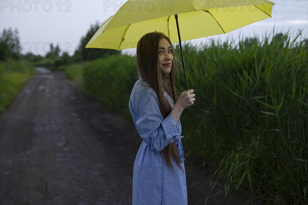 Russia, Omsk, Portrait of young woman with umbrella on dirt road