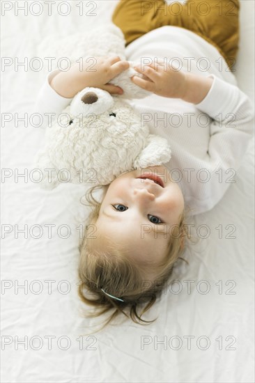 Smiling toddler girl lying on bed with teddy bear toy