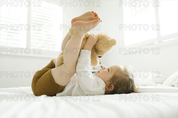 Toddler girl lying on bed with her teddy bear toy