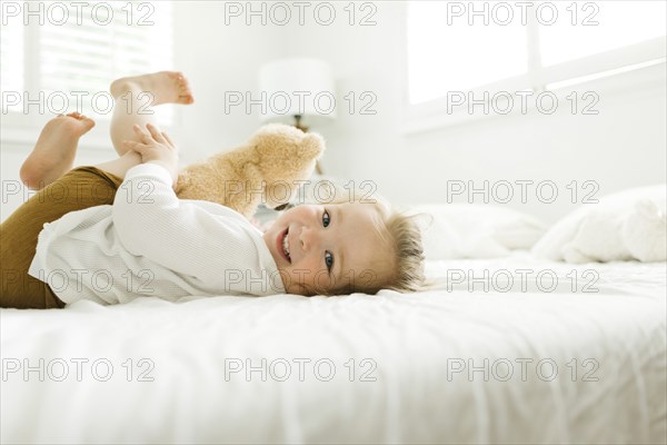 Toddler girl lying on bed with her teddy bear toy