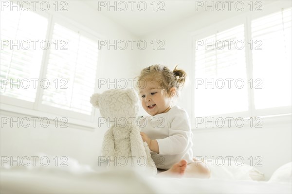 Toddler girl playing on bed with her teddy bear toy