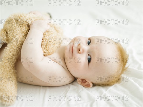 Portrait of baby boy lying on bed with teddy bear