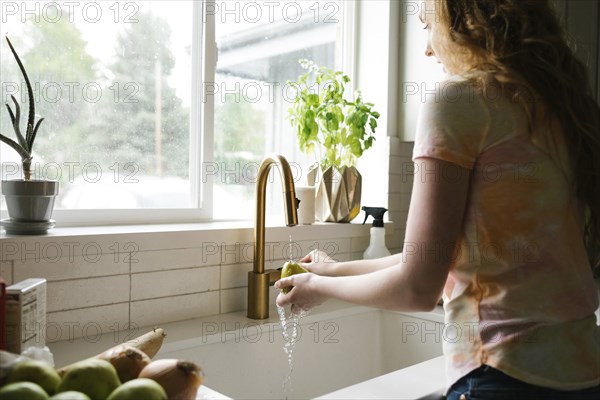 Woman washing pear in kitchen