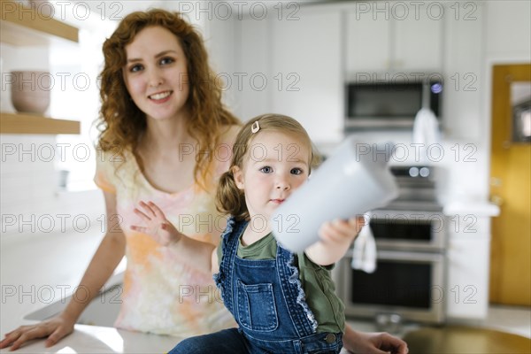 Girl (2-3) sitting on kitchen counter next to mother and holding sippy cup