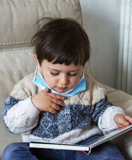 Boy (2-3) wearing face mask holding book