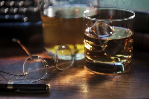 Whiskey glass and eyeglasses next to typewriter on desk