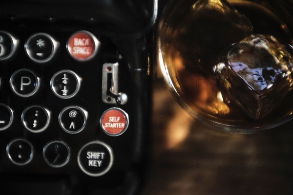 Whiskey glass next to typewriter on desk