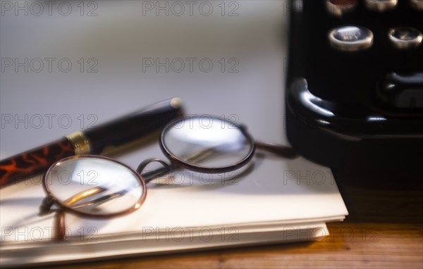 Retro eyeglasses and pen on stack of paper next to typewriter