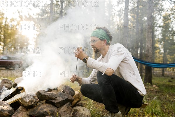 Man with marshmallow crouching at campfire, Wasatch Cache National Forest