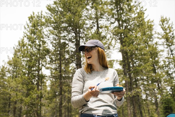 Smiling woman holding plate on camping in forest, Wasatch-Cache National Forest