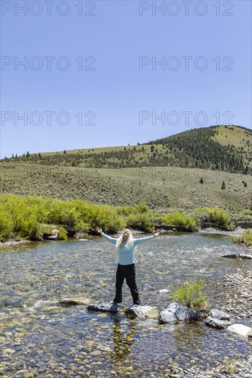 USA, Idaho, Sun Valley, Woman with arms raised standing on rocks in river