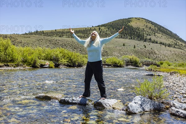 USA, Idaho, Sun Valley, Woman with arms raised standing on rocks in river