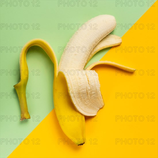 Half peeled banana on green and yellow background