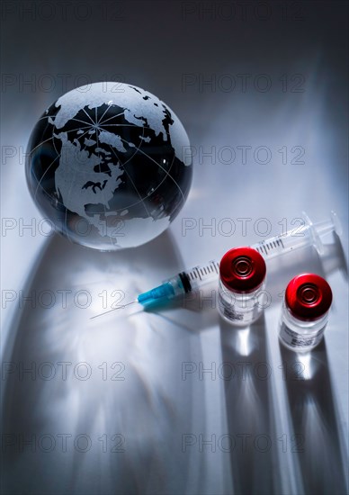 Glass globe and syringe with vaccine on gray background