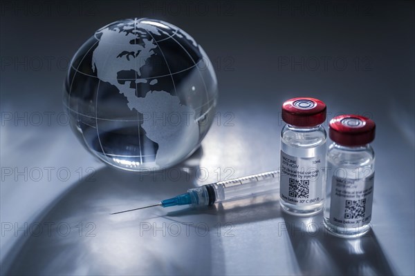 Glass globe and syringe with vaccine on gray background