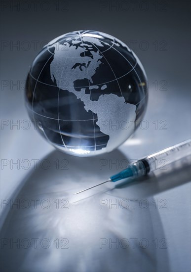 Glass globe and syringe on gray background