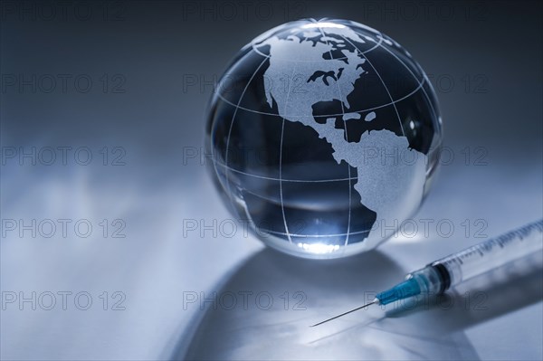 Glass globe and syringe on gray background