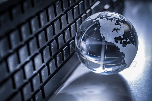 Glass globe and computer keyboard on gray background