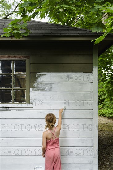 Girl (6-7) painting cottage wall