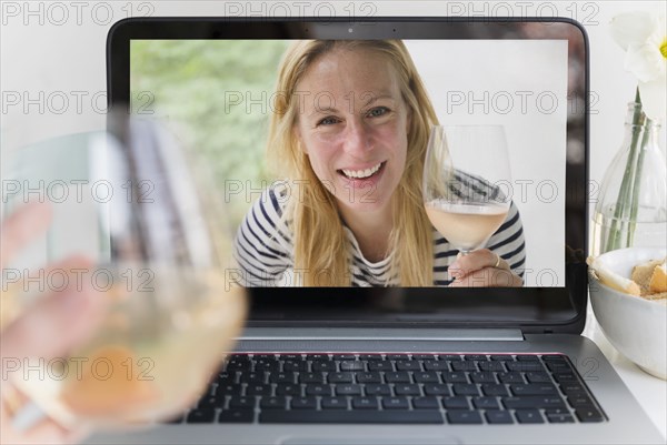 Woman drinking wine with friend online