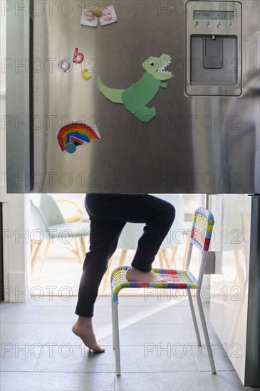 Boy (4-5) using chair while searching for food in fridge